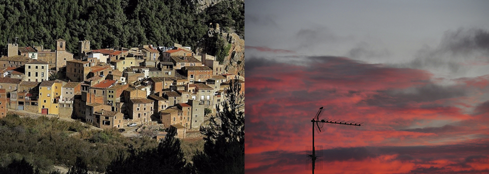 Un pueblo en la ladera de una colina con edificios de color tostado se sitúa junto a un cielo al atardecer con nubes rojas y una antena de televisión en silueta.